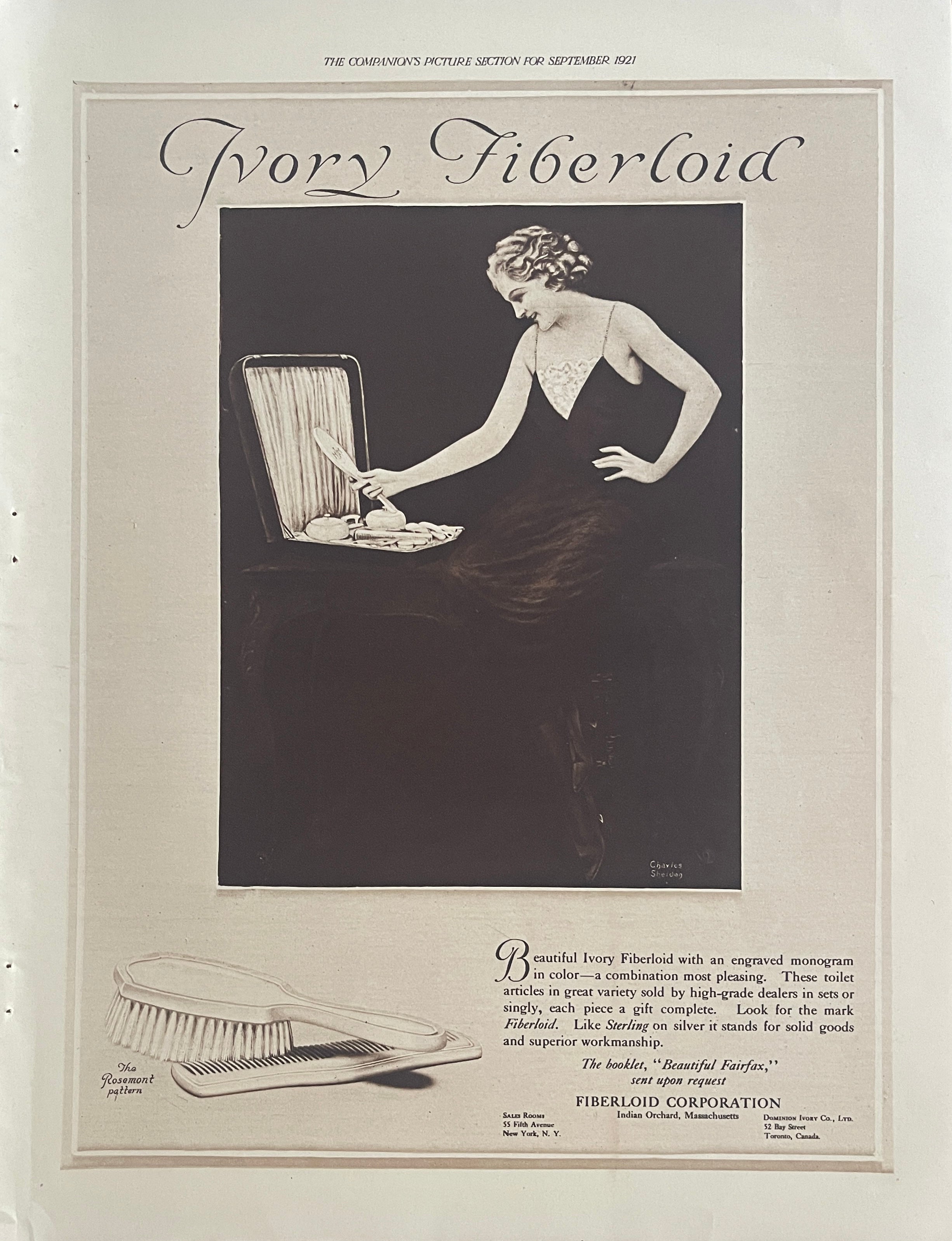 1921 Ivory Fiberloid vintage magazine advertisement featuring an elegant woman with a vanity set and monogrammed grooming accessories by Fiberloid Corporation.